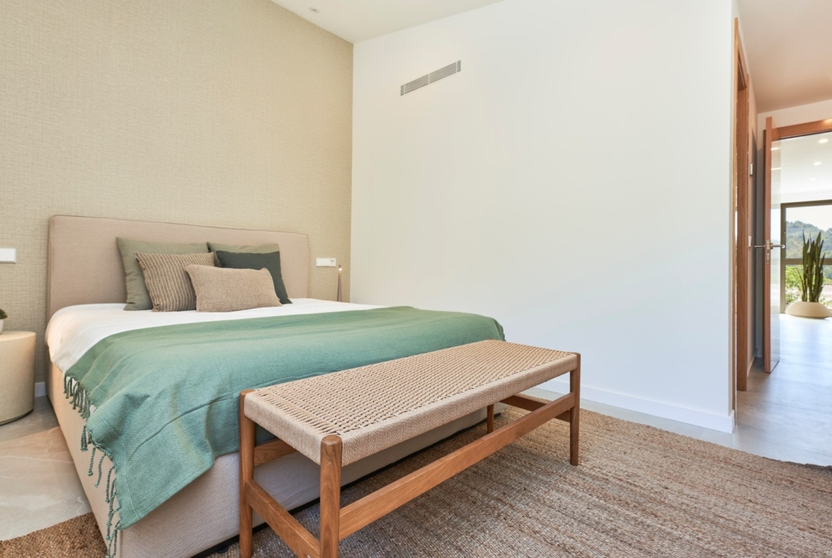 Sypialnia w inwestycji ES Voltor: łóżko z zieloną narzutą, ławka u wezgłowia i korytarz z wyjściem na ogród.