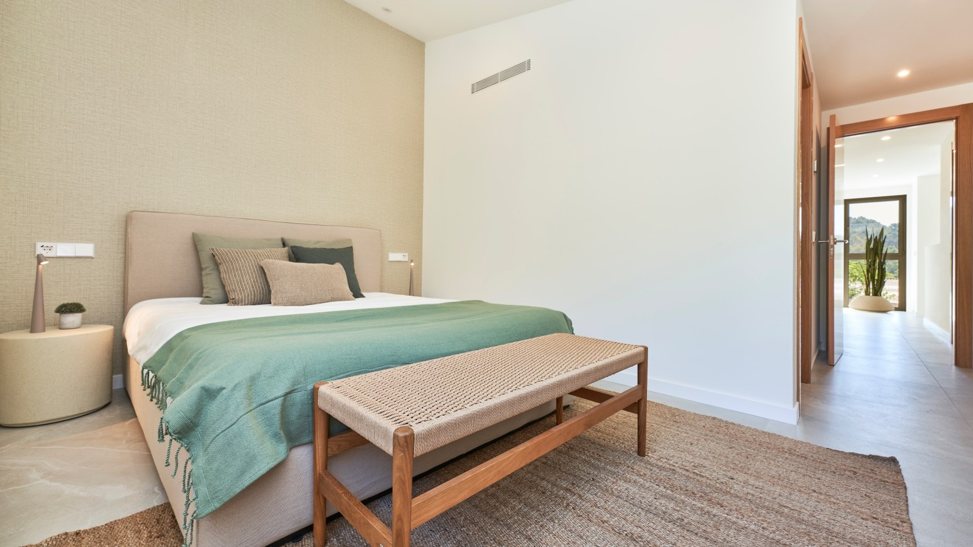 Sypialnia w inwestycji ES Voltor: łóżko z zieloną narzutą, ławka u wezgłowia i korytarz z wyjściem na ogród.