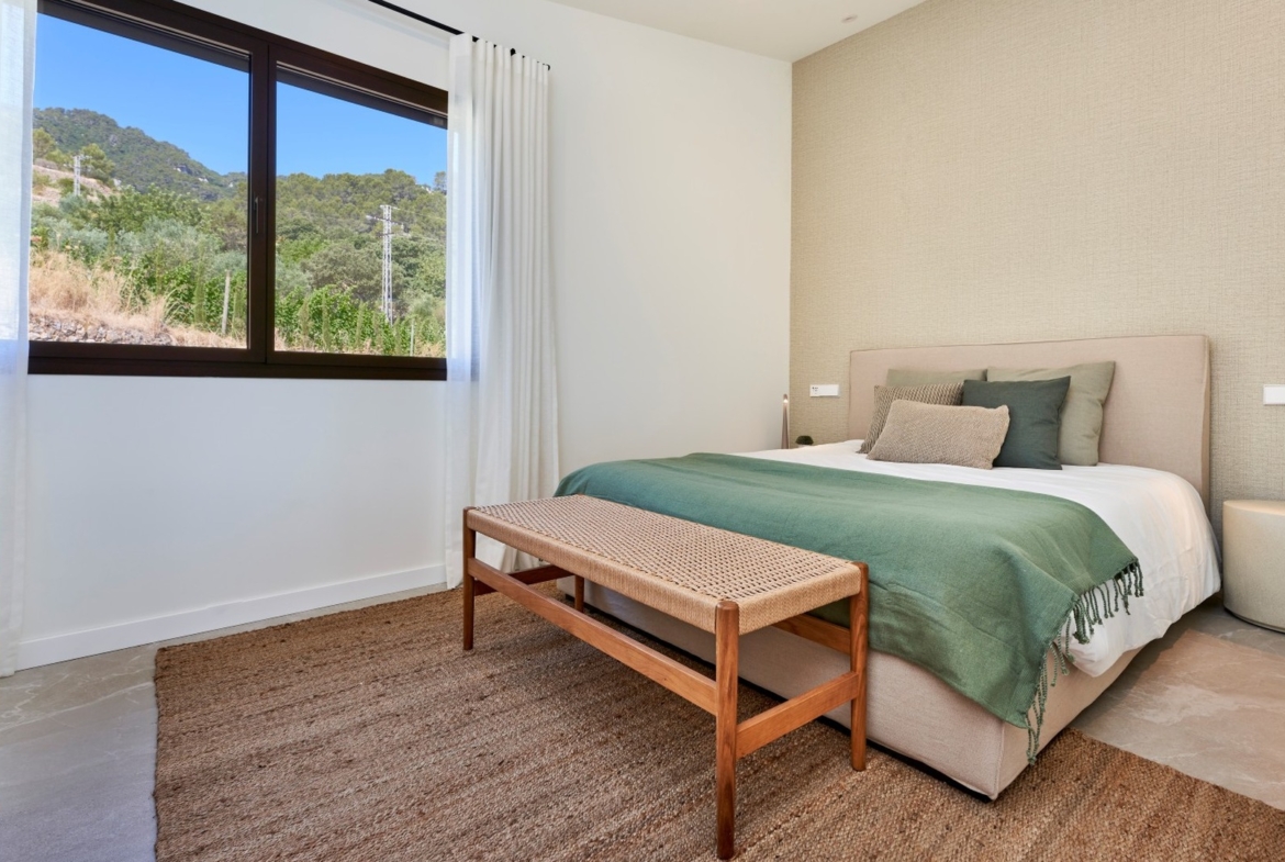 Sypialnia w ES Voltor z szerokim oknem, łóżkiem małżeńskim i plecioną ławką u wezgłowia.