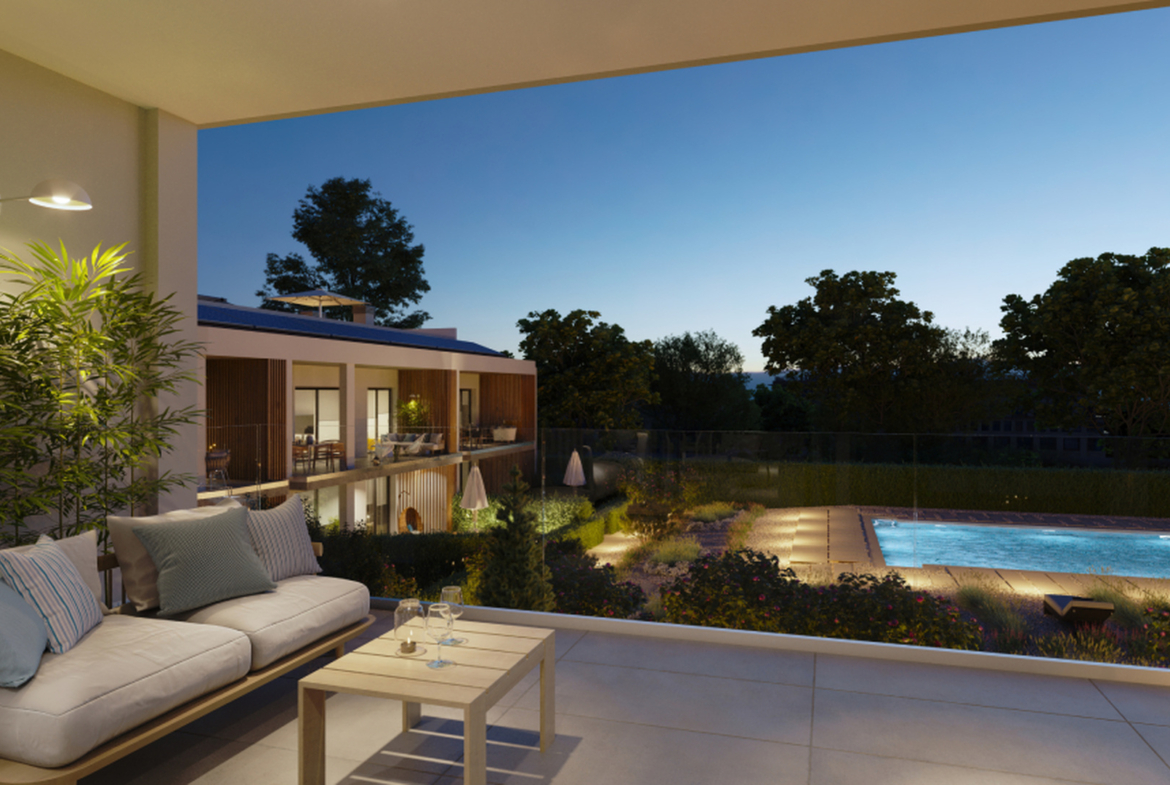 Zadaszony balkon z sofą i widokiem na podświetlony basen nocą.